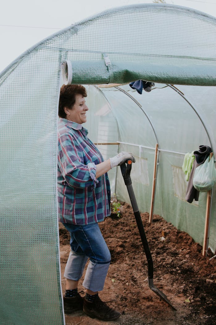 featured-portfolio-04 Smiling woman working with a spade inside a greenhouse, engaged in gardening activities.
